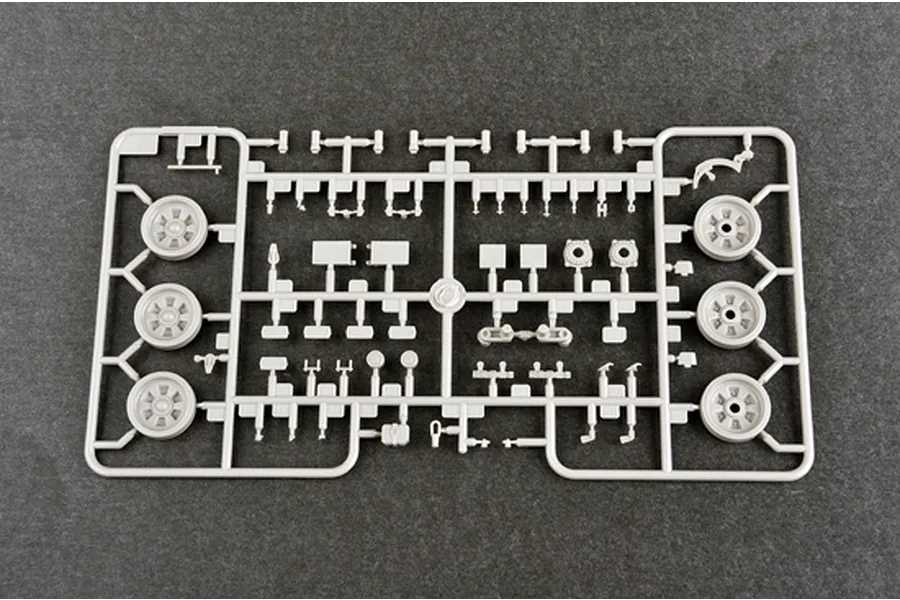 A grey plastic model kit sprue containing various tank parts including wheels and small mechanical components on a dark textured background.