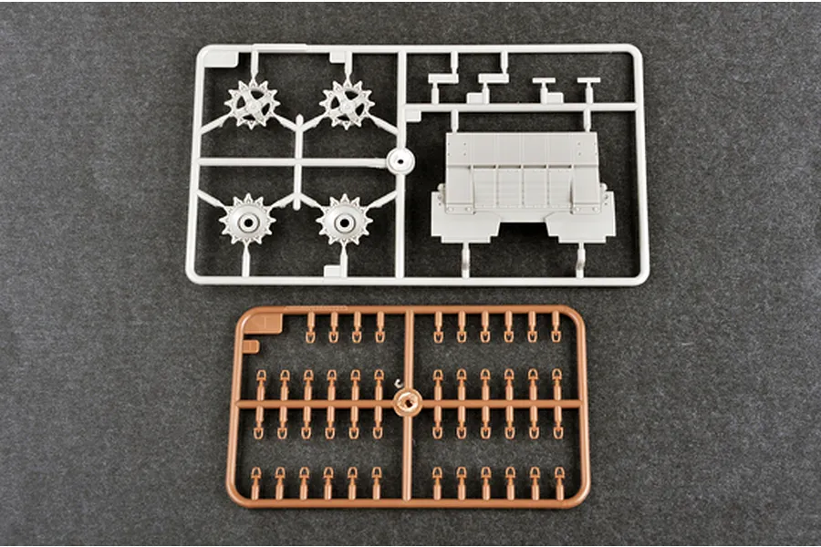 Two plastic model kit sprues on a dark grey background, one light grey with tank parts and one brown with small connector pieces.