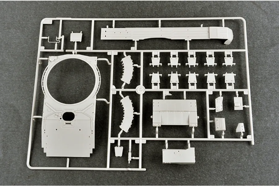 A grey plastic model kit sprue containing various tank parts, including a turret ring and hull components, on a dark grey surface.