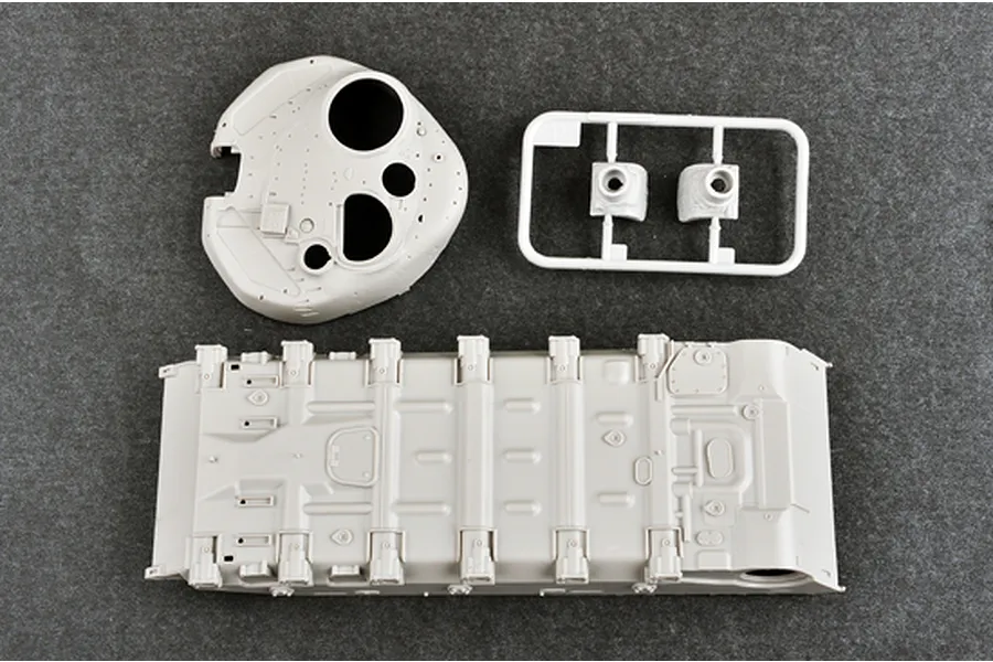 Unassembled plastic model tank parts including the main hull and turret shell on a grey background.