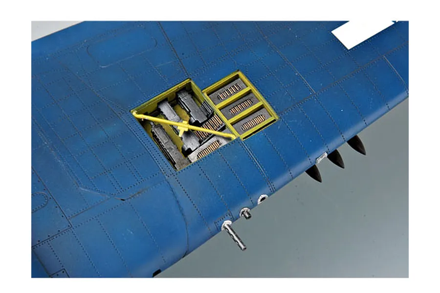 Close-up of a blue aircraft wing model showing an open gun bay with ammunition belts and internal mechanisms visible.