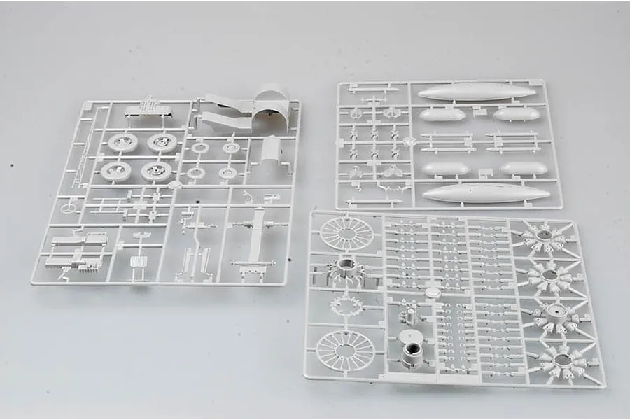 Three grey plastic model kit sprues containing various aircraft parts like wheels, engine cylinders, and fuel tanks on a white background.