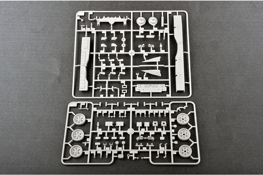 Two grey plastic model kit sprues containing various tank parts, including wheels and suspension components, laid out on a dark grey surface.
