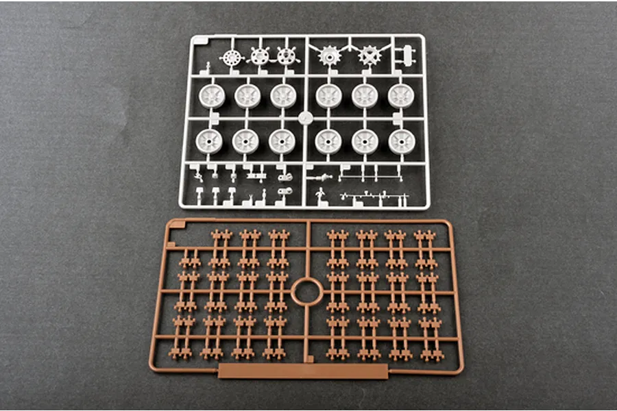 Two plastic model kit sprues on a dark grey background, one grey with wheels and one brown with track links.