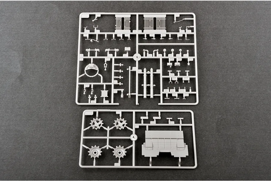 Two grey plastic model kit sprues containing various tank parts, including sprocket wheels and hull sections, laid out on a dark grey surface.