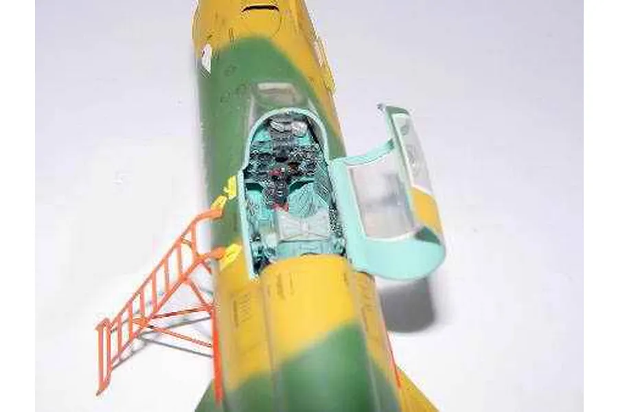 Top-down view of a partially assembled MiG-21 model aircraft showing the detailed cockpit, open canopy, and an orange access ladder.