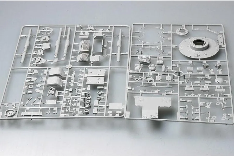 Two grey plastic model kit sprues containing various tank parts, including a turret top, gun barrels, and small accessories, laid out on a plain background.