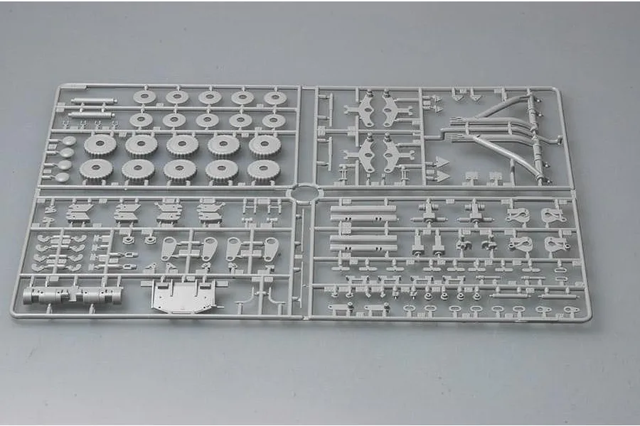 A grey plastic model kit sprue containing various tank parts including wheels, suspension arms, and structural components on a plain background.