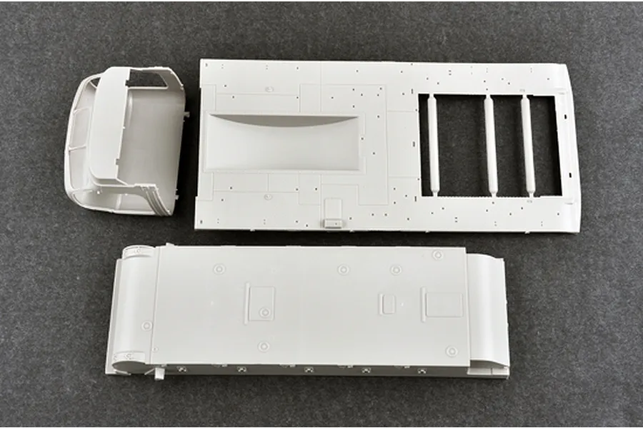 Unassembled grey plastic model kit parts for a military vehicle, including a truck cab and chassis components, viewed from above on a dark grey surface.
