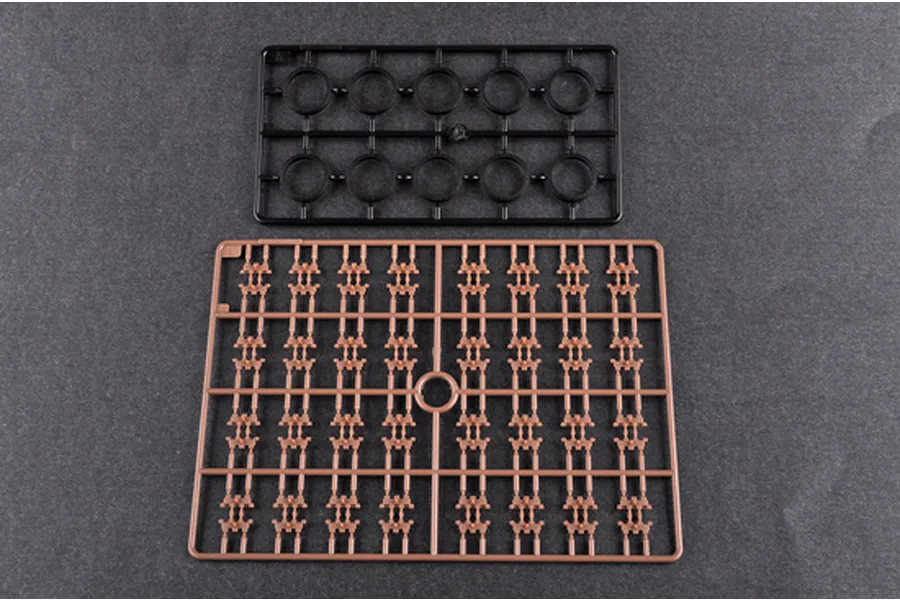 Two plastic model kit sprues on a dark grey background, one black with circular parts and one tan with small track-like components.