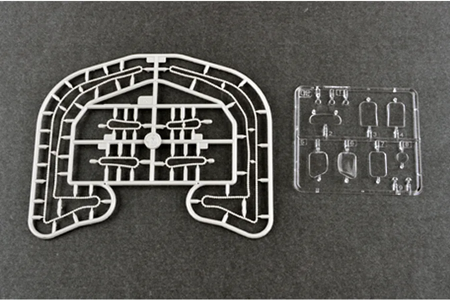 Two plastic model kit sprues on a dark grey background, one grey and one clear, containing small vehicle parts.