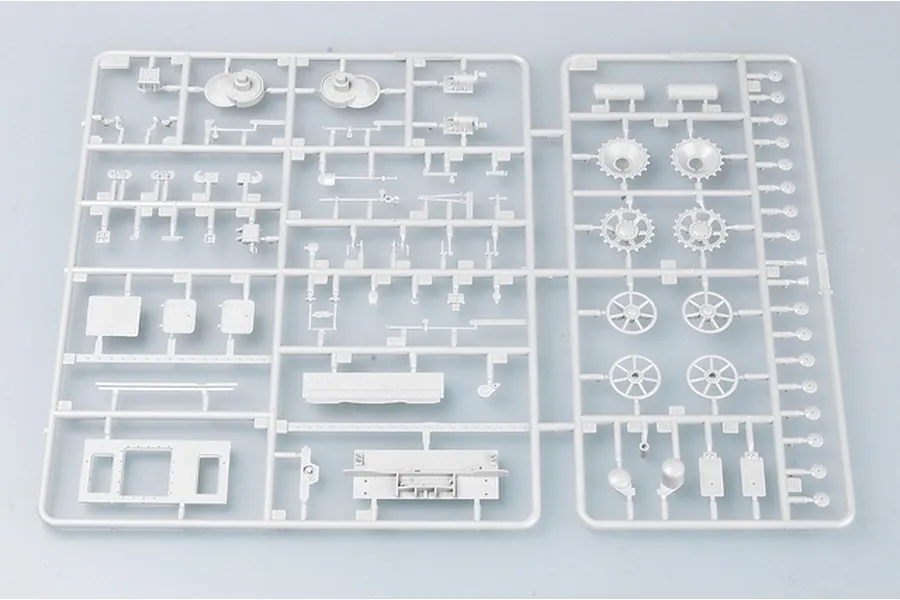 A grey plastic sprue containing various unpainted model tank parts, including wheels, sprockets, and hull components for a 1/35 scale model kit.