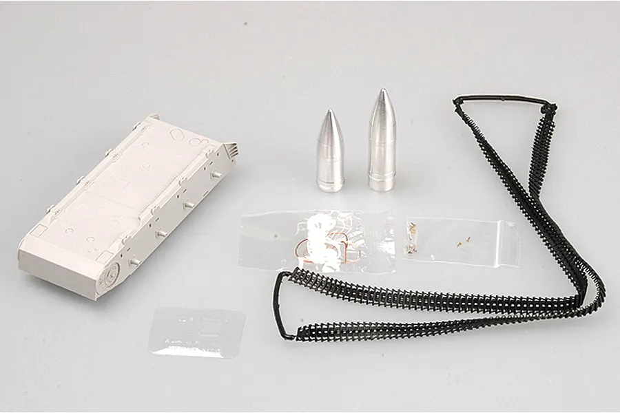 Components for a 1/35 scale model kit including a grey plastic tank hull, two metal shells, black plastic tank tracks, and small hardware bags.