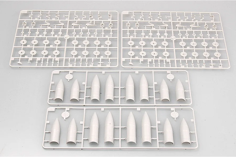 Four grey plastic model kit sprues containing tank suspension parts and cylindrical components on a plain background.