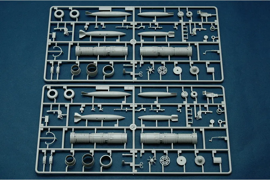 Two identical grey plastic model kit sprues containing aircraft parts like engine components, missiles, and landing gear wheels on a dark blue background.