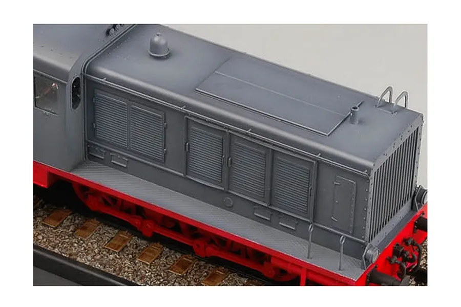 A high-angle close-up of a grey and red German WR 360 C12 locomotive model kit on a gravel track base.