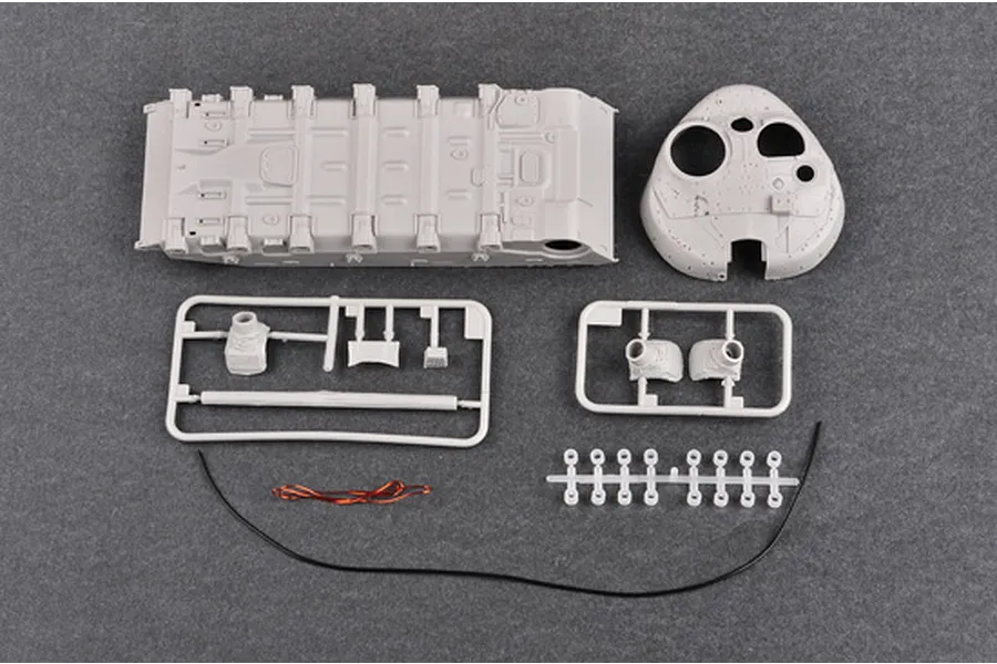 Unassembled plastic model tank parts including the hull, turret, and sprues on a grey background.