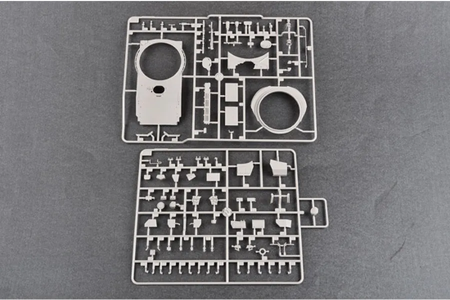 Two grey plastic model kit sprues containing various tank parts, including a turret top, laid out on a dark grey surface.