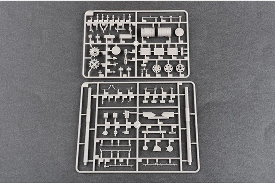 Two grey plastic model kit sprues containing various tank parts, including wheels and gun barrels, laid out on a dark grey surface.