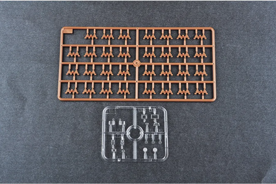 Two plastic model kit sprues on a dark grey background, one brown with many small parts and one clear with smaller components.