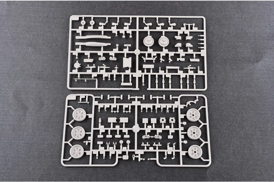 Two grey plastic model kit sprues containing various tank parts, including wheels and suspension components, laid out on a dark grey surface.