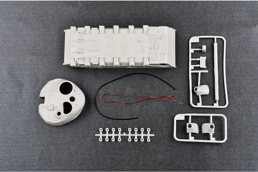 Unassembled plastic model tank parts including the hull, turret, and sprues on a dark grey background.