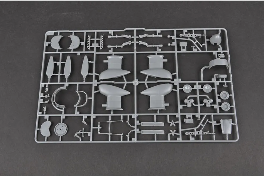 A grey plastic model kit sprue containing various aircraft parts, including propeller blades and landing gear fairings, on a dark background.