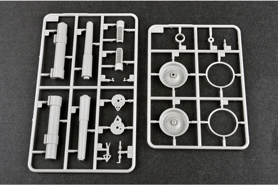 Two grey plastic model kit sprues containing artillery parts, wheels, and gun barrels on a dark grey surface.