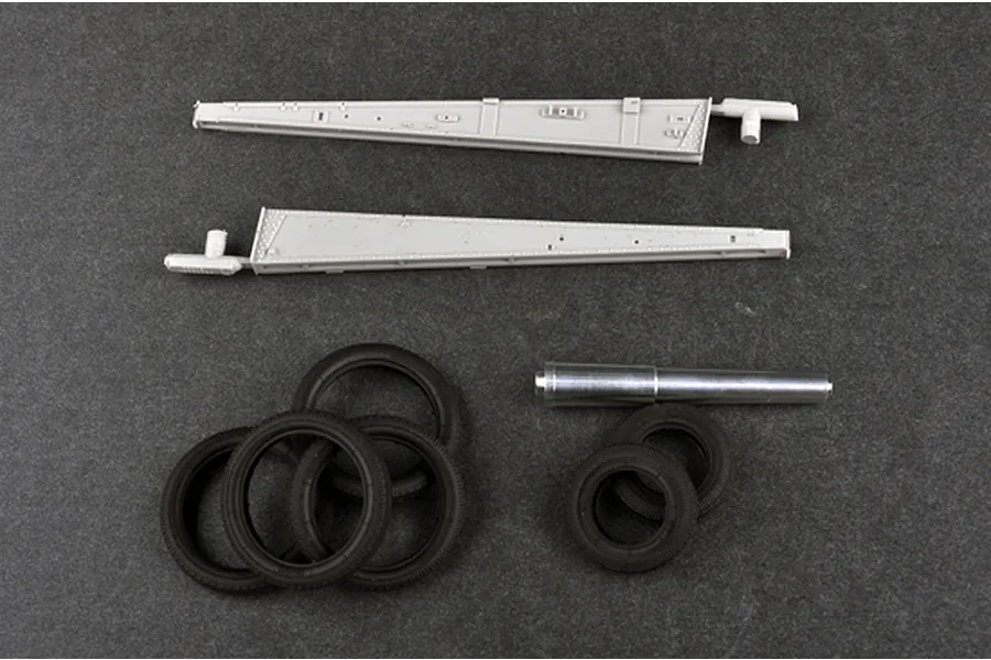 Plastic model kit parts including two long grey trail arms, five black rubber tires, and a metal gun barrel for a 1/35 scale artillery model.