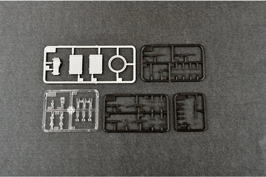 Four plastic model kit sprues on a dark grey background, including one light grey, two dark brown, and one clear plastic sprue.