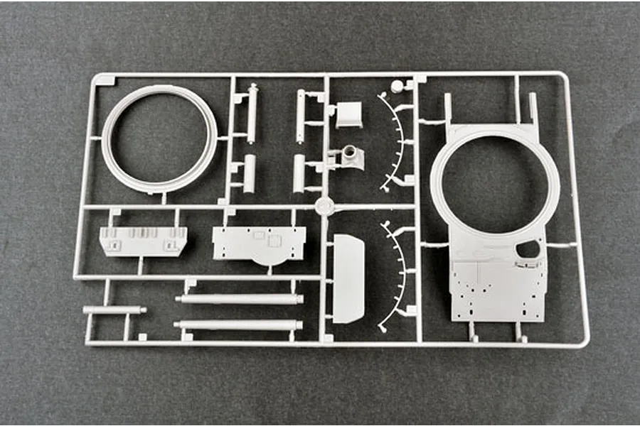 A grey plastic sprue containing various model tank parts, including a turret ring and hull components, on a dark grey background.