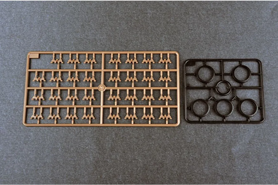 Two plastic model kit sprues on a dark grey background, one tan sprue with small parts and one black sprue with circular parts.