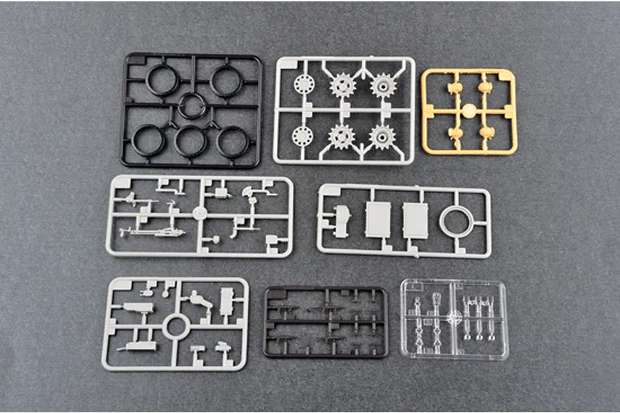 Several plastic model kit sprues for a tank model, including grey, black, tan, and clear parts on a grey background.