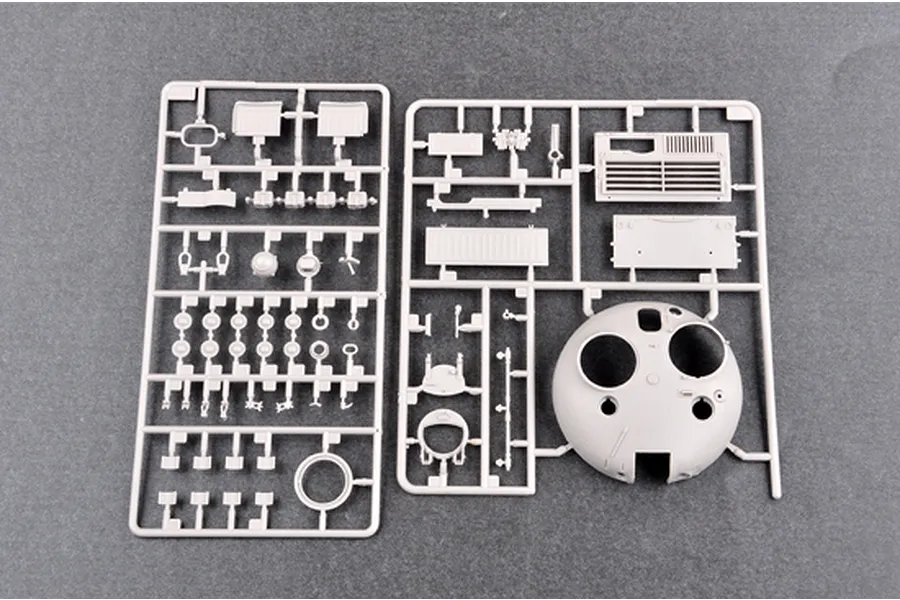 Two grey plastic model kit sprues containing various tank parts, including a turret shell, laid out on a dark grey surface.
