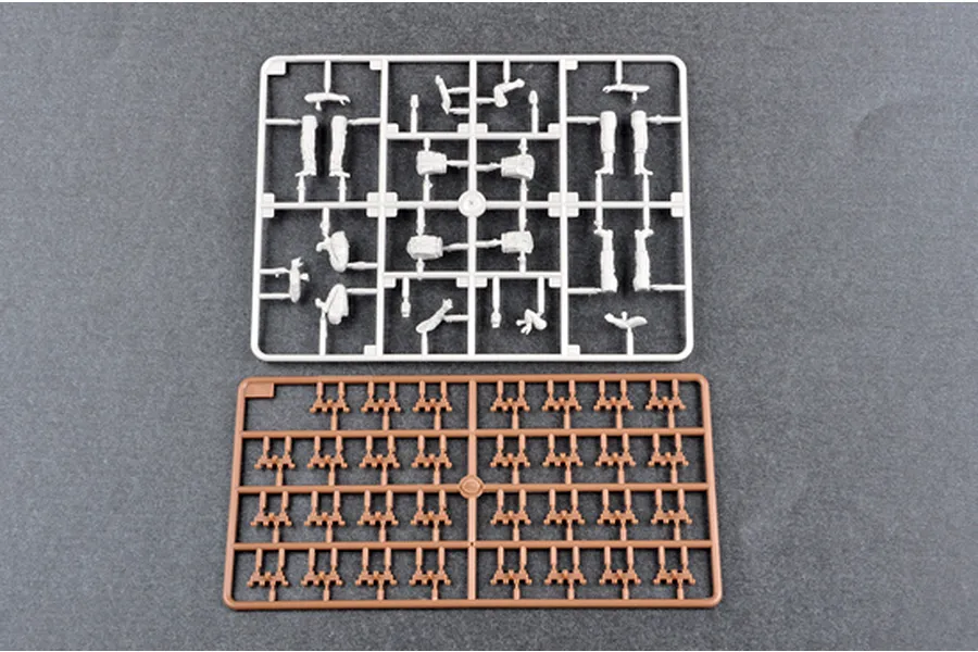Two plastic model kit sprues on a grey background, one white with figure parts and one brown with small track or suspension components.