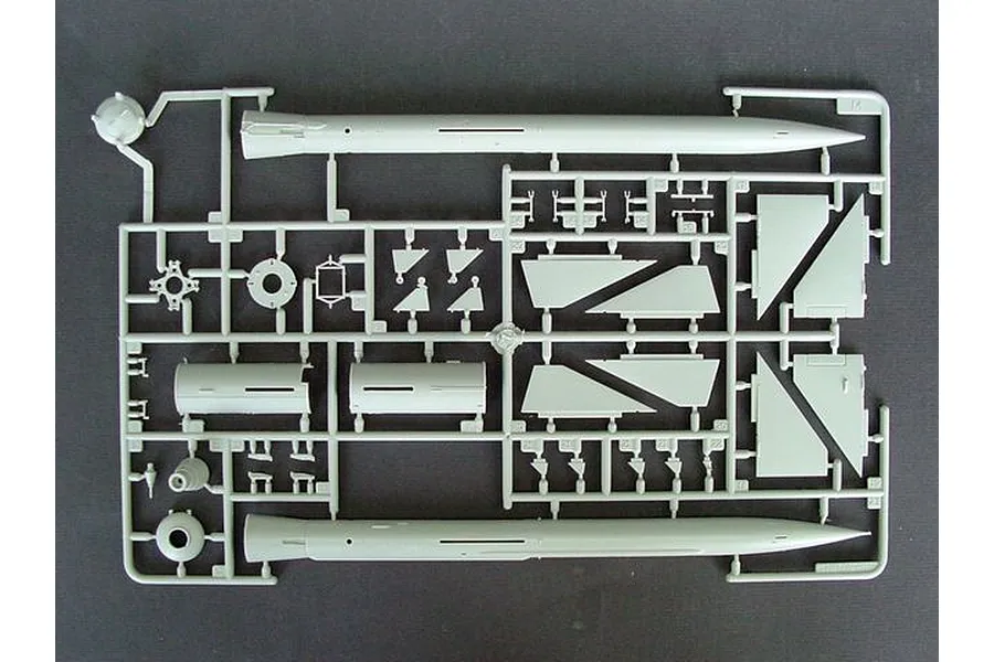 A grey plastic model kit sprue containing parts for a missile, including the main body sections and various fins, on a dark background.
