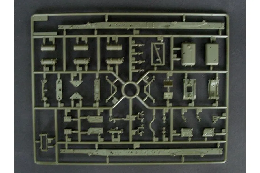 A single olive green plastic sprue containing various model kit parts for a military vehicle, viewed from directly above against a dark background.
