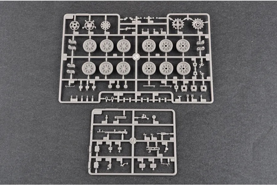 Two grey plastic model kit sprues containing tank wheels, sprockets, and small mechanical parts on a dark grey background.