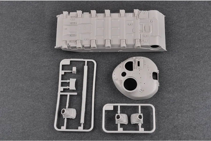 Unassembled grey plastic model kit parts for a tank, including the lower hull, turret, and sprue frames on a dark grey background.
