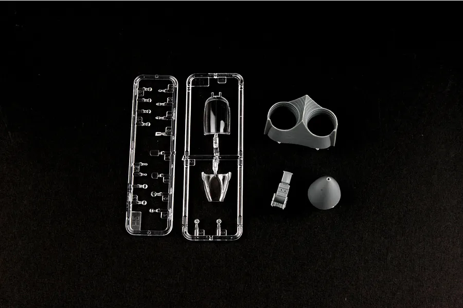 Plastic model kit parts including clear canopy sprues and grey plastic components for a fighter jet model on a black background.