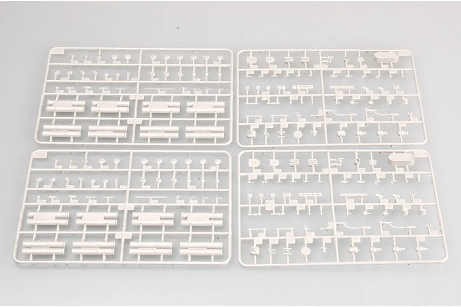 Four grey plastic model kit sprues arranged on a light grey background, featuring various small ship parts and cylindrical components.