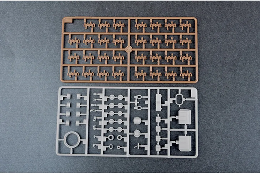 Two plastic model kit sprues on a dark grey background, one brown and one grey, containing various small tank parts.