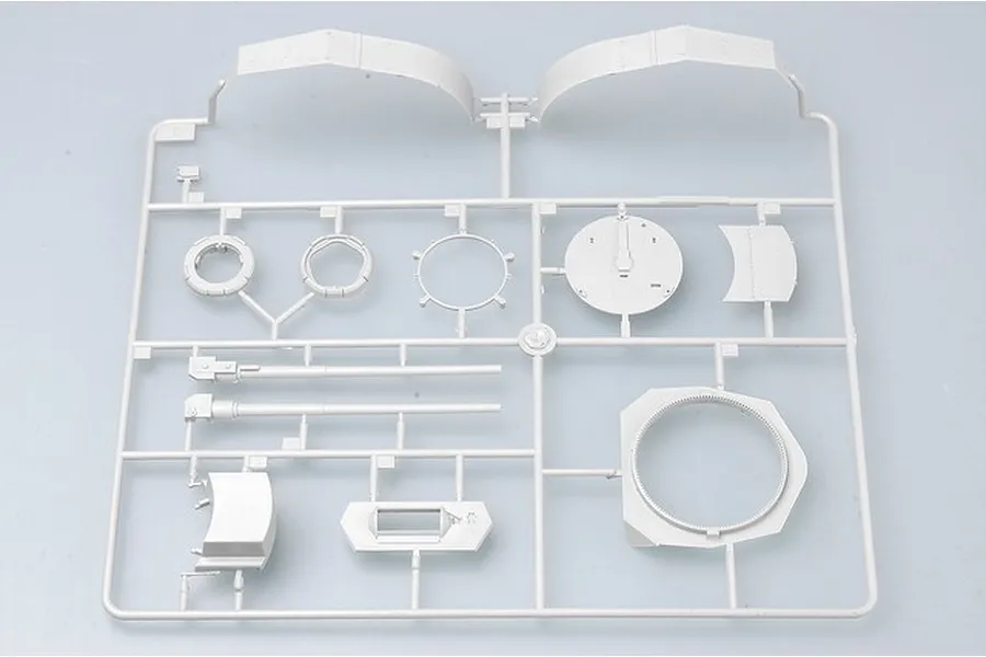 A light grey plastic model kit sprue containing various parts for a military vehicle model, including gun barrels, turret rings, and curved armor plates.