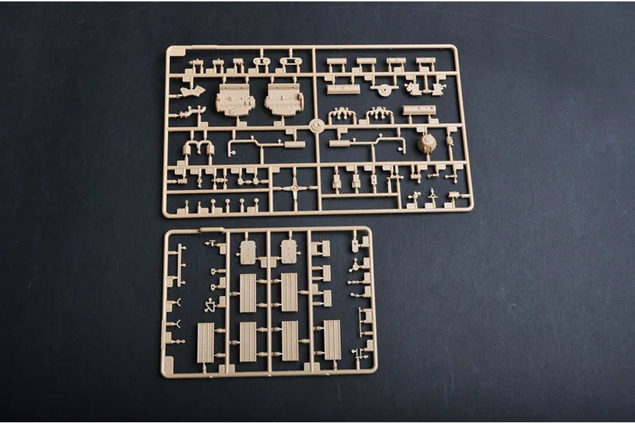 Two tan plastic model kit sprues containing various vehicle parts laid out on a dark surface.