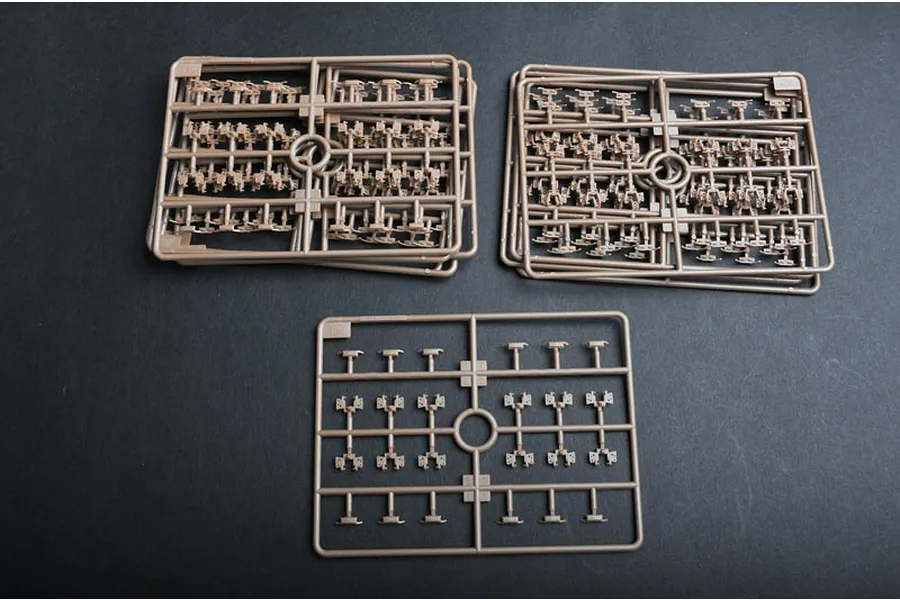Three light brown plastic model kit sprues containing small tank track link parts on a dark grey background.