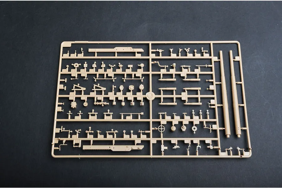 A tan plastic model kit sprue containing various small parts and two long gun barrels for a 1/35 scale military vehicle model.