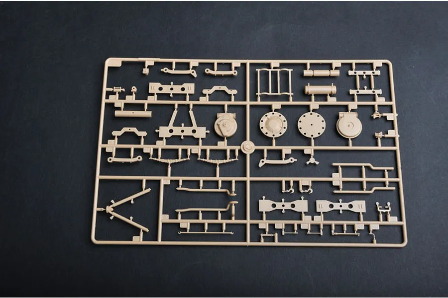 A tan plastic model kit sprue containing various vehicle suspension and chassis parts for a 1/35 scale military model.