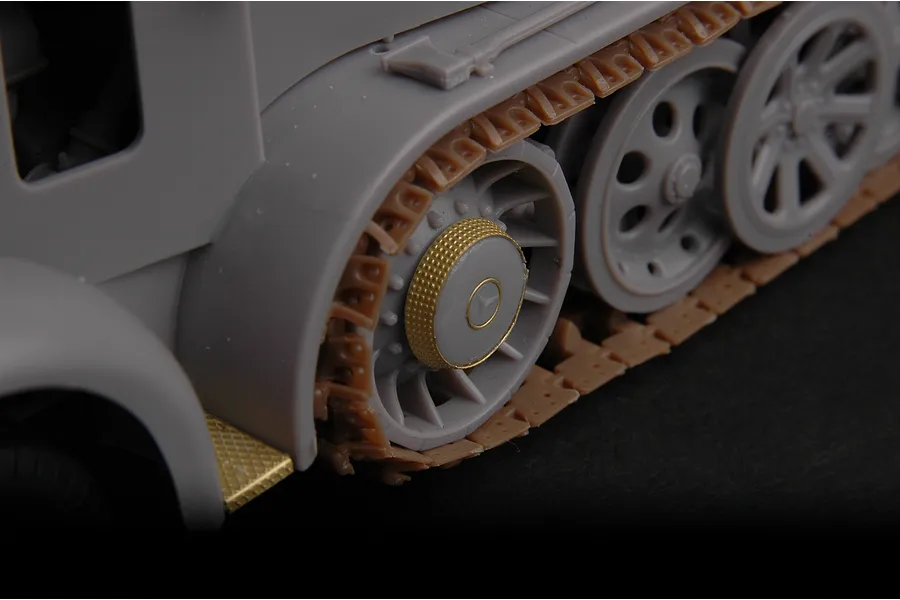 Close-up of a plastic model half-track vehicle showing grey wheels, brown tracks, and gold-coloured photo-etched metal detail parts.