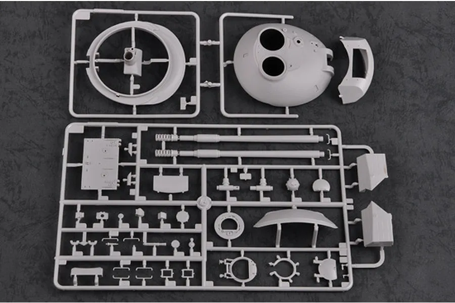 Two grey plastic model kit sprues containing tank turret and gun barrel parts on a dark textured background.