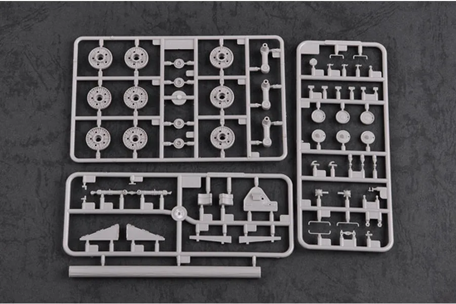Three grey plastic model kit sprues containing tank wheels and small mechanical parts on a dark textured background.